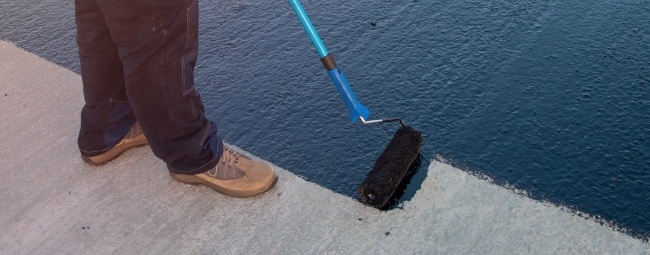 Man applying black roof coating to a concrete roof